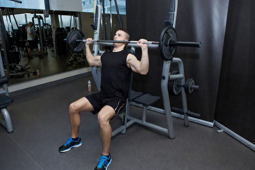 Man performing a barbell shoulder press in a gym